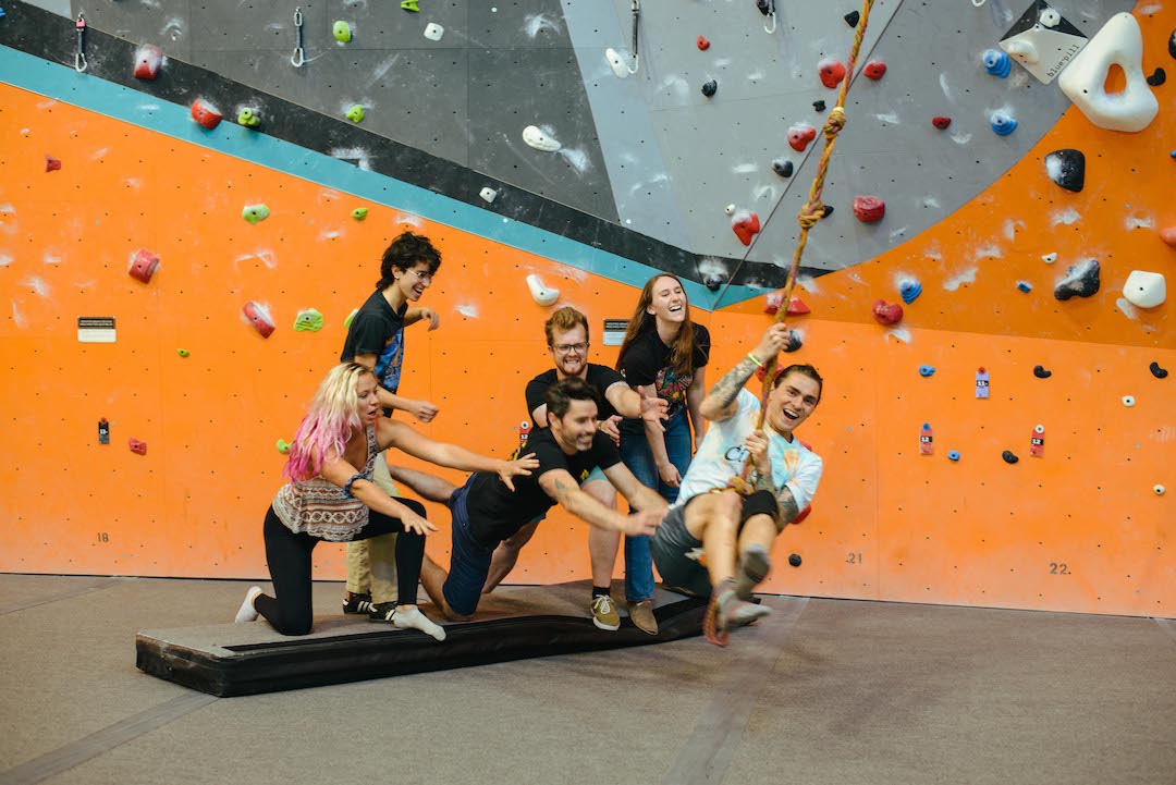 Man swinging on rope swing with team members helping and smiling.